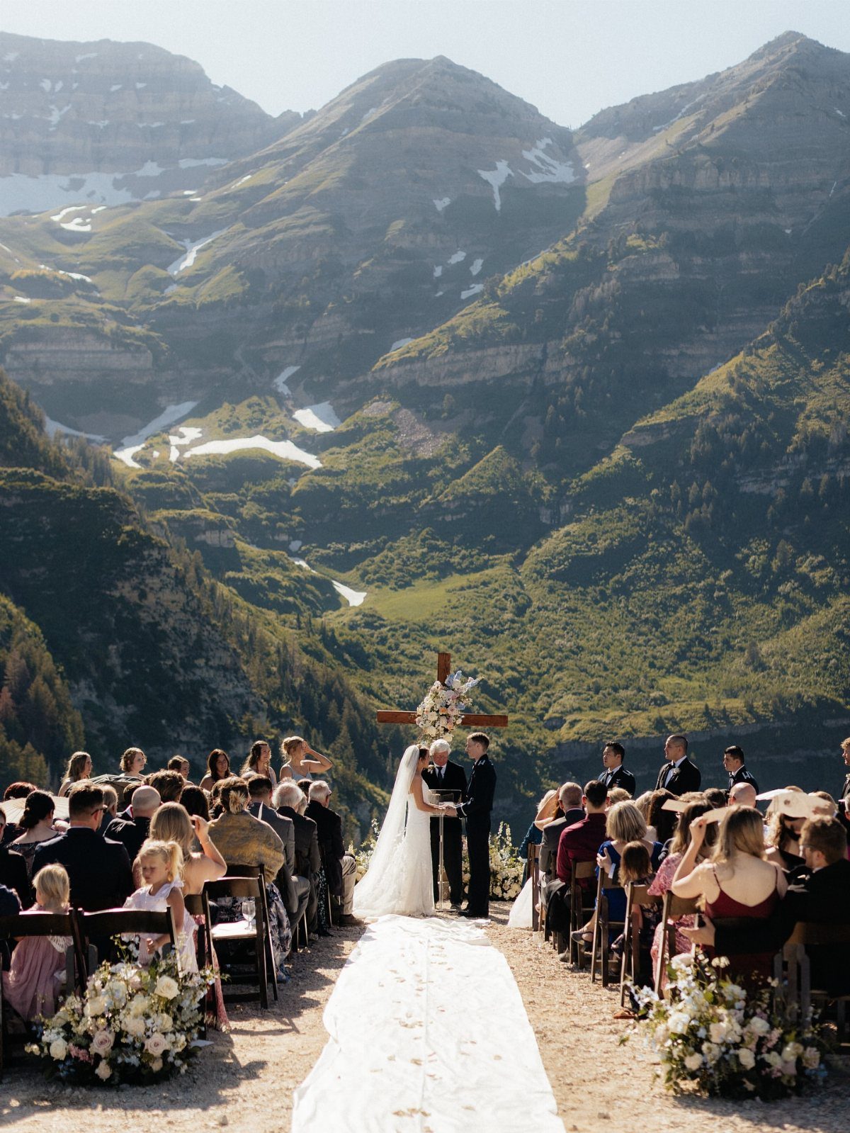 Wedding ceremony with a white aisle and guests before a mountain backdrop.