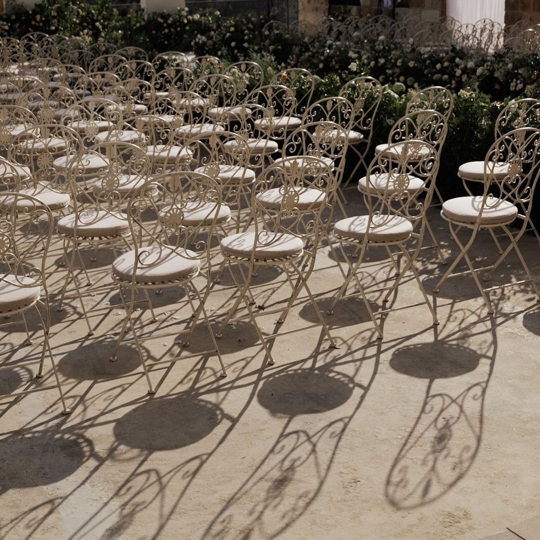 White ornate metal chairs arranged for an outdoor wedding ceremony on a stone patio