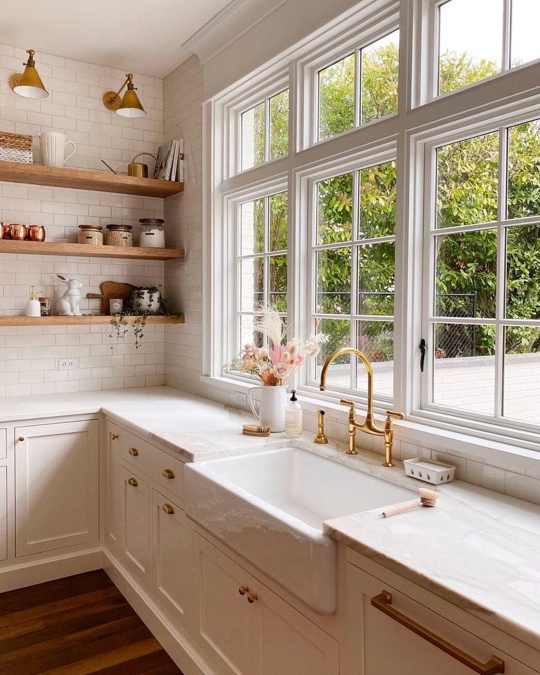 White farmhouse sink with gold faucet in a bright, rustic kitchen setting.