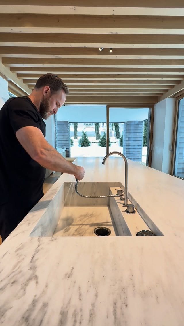 Man using a silver faucet at a white marble integrated kitchen sink island.