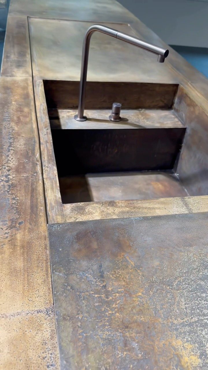 Dark metallic integrated sink with a curved bronze faucet in a rustic countertop
