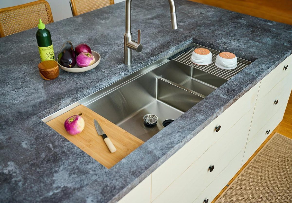 Stainless steel low divide sink in a dark grey stone kitchen countertop.