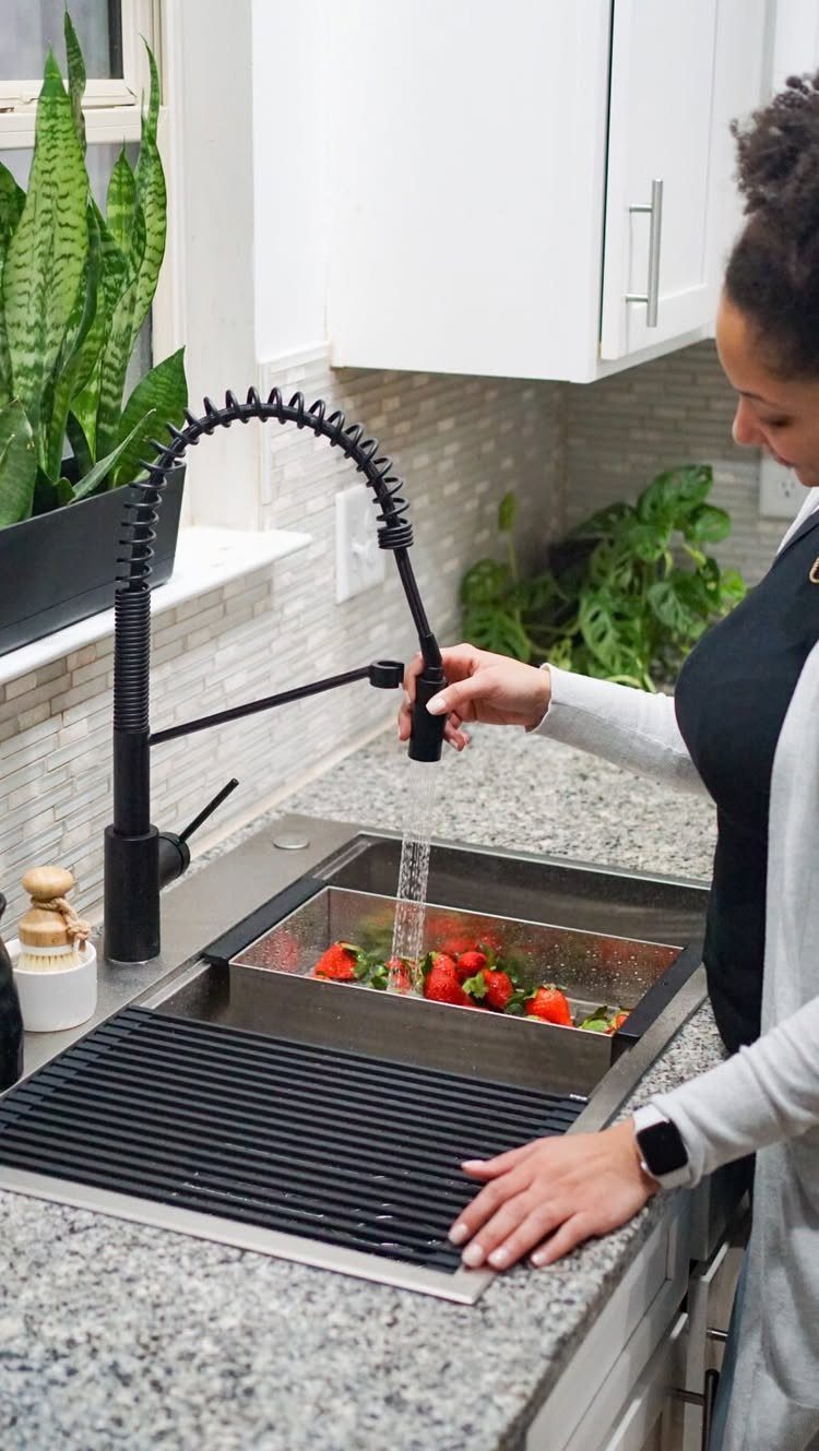 Single basin stainless steel kitchen sink with black faucet and strawberries being washed.