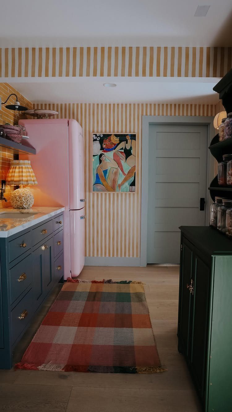 Pink refrigerator in a kitchen with yellow striped wallpaper and a small table lamp.