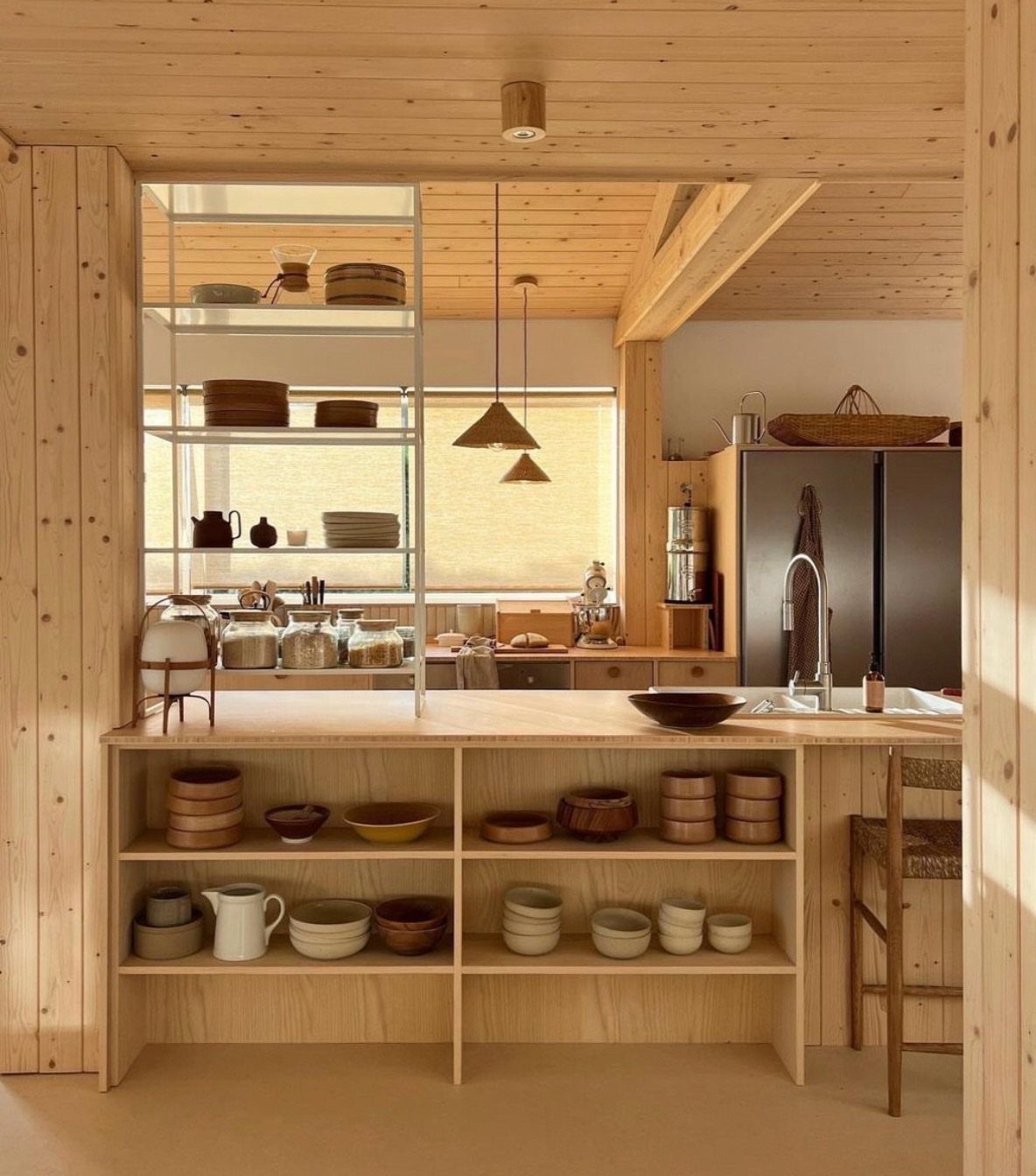 Two small cone-shaped wooden pendant lights hanging in a light-wood minimalist kitchen.