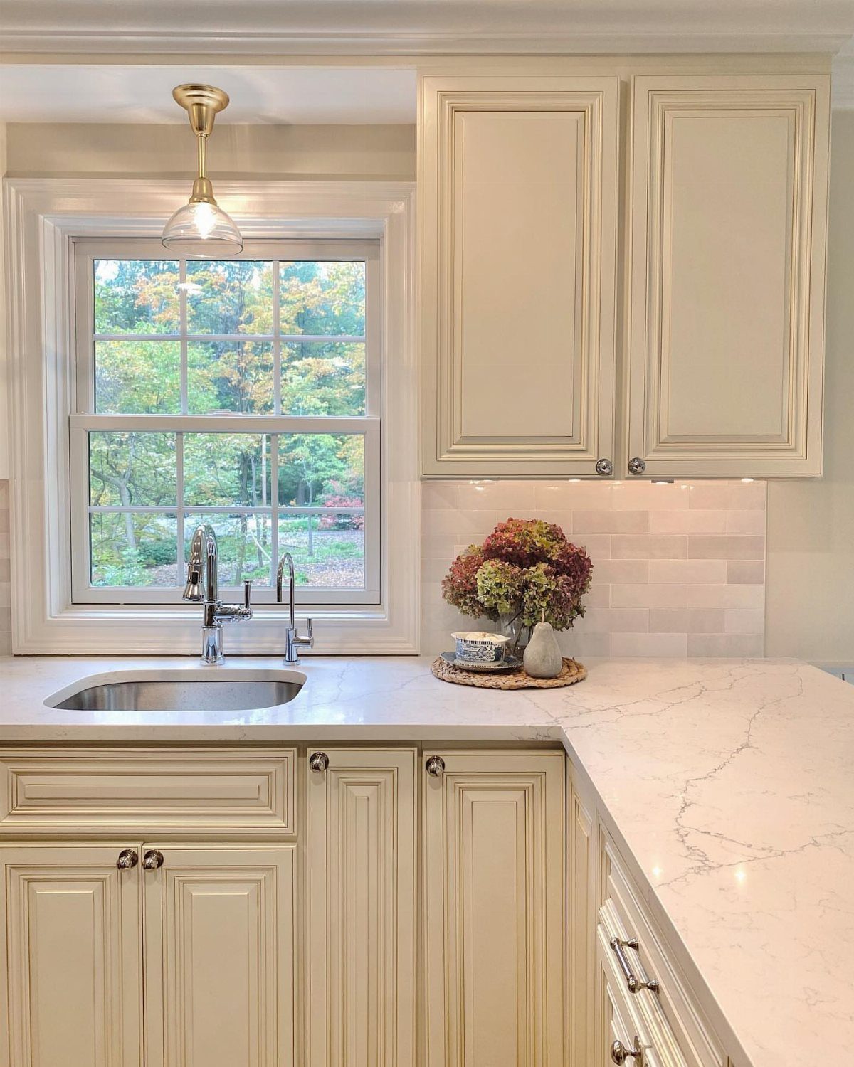 Gold pendant light hanging above a kitchen sink in front of a window