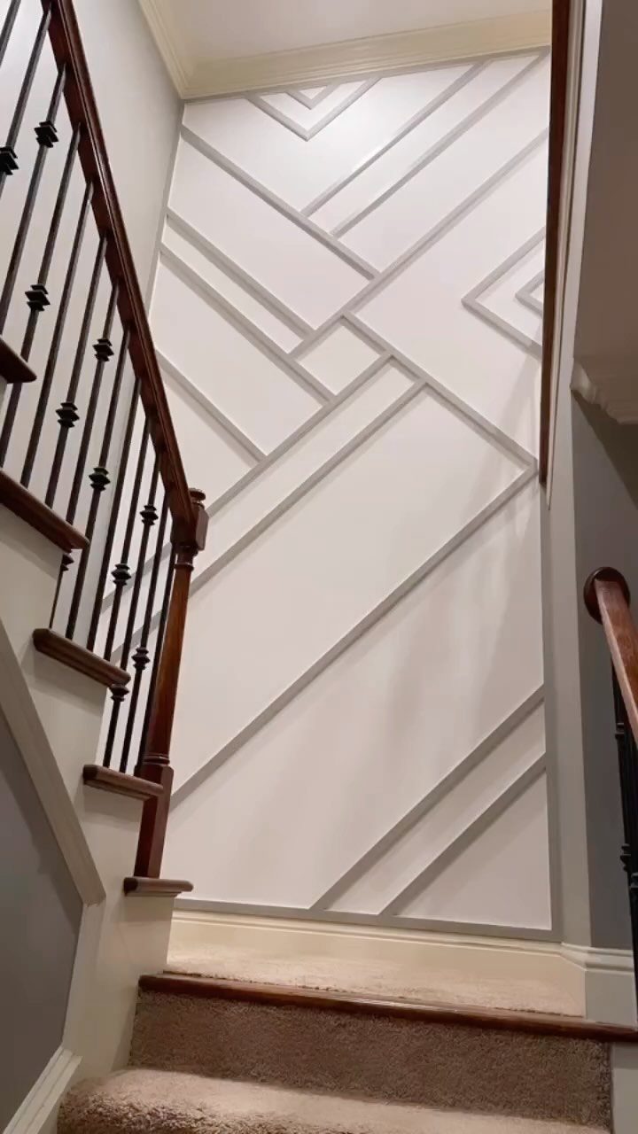 White accent wall with asymmetrical geometric wood slats in a residential stairwell.