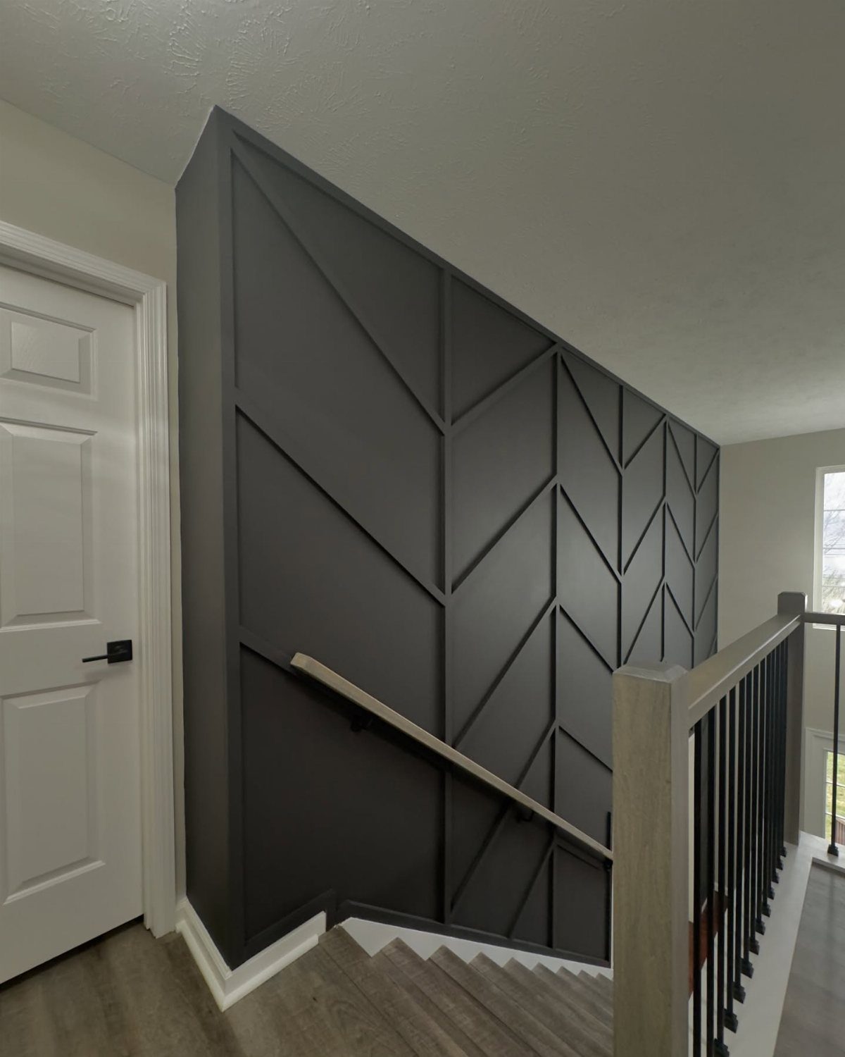 Dark grey stairwell accent wall with a geometric chevron wood molding pattern.