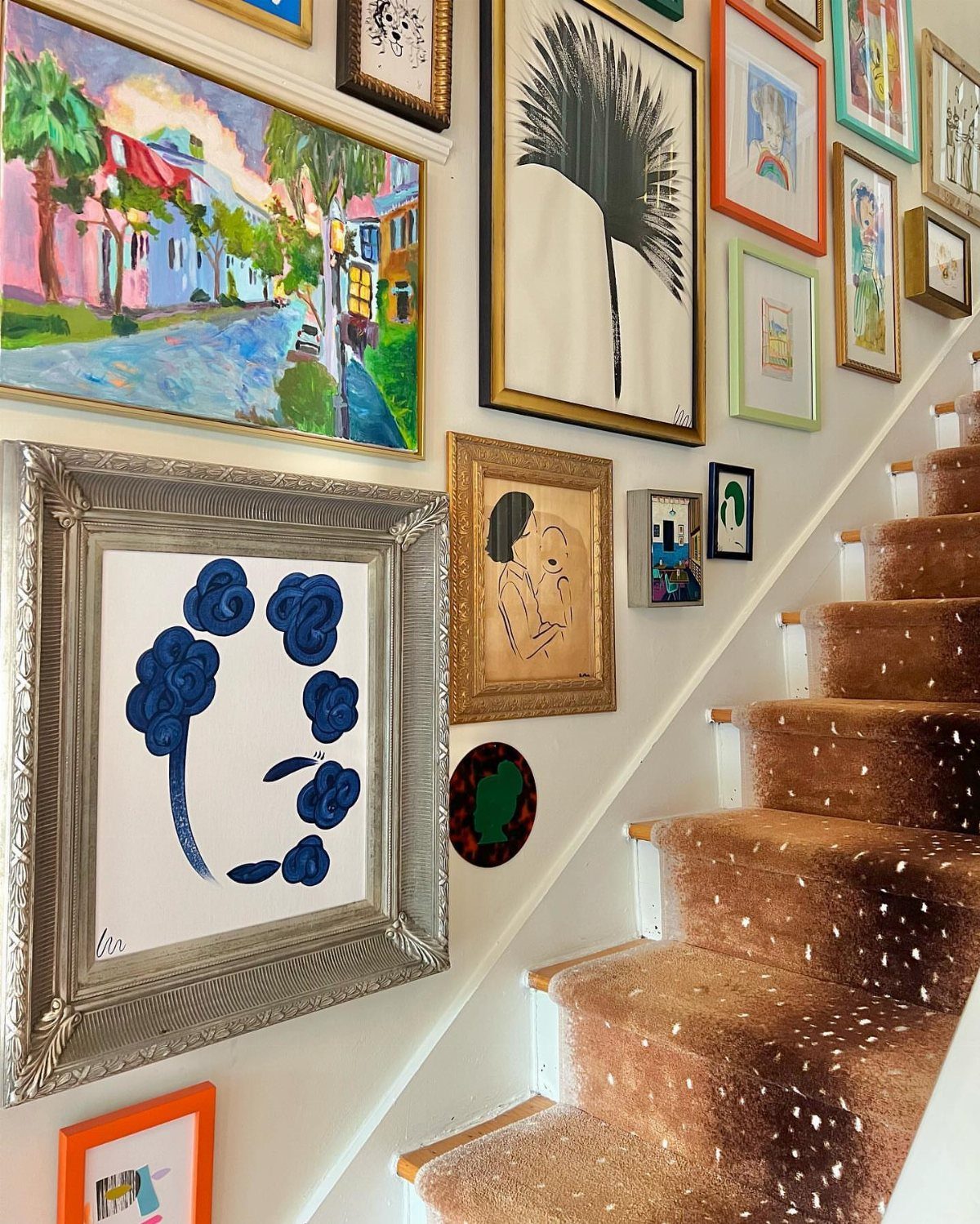 Gallery wall with diverse framed art along a brown carpeted staircase.
