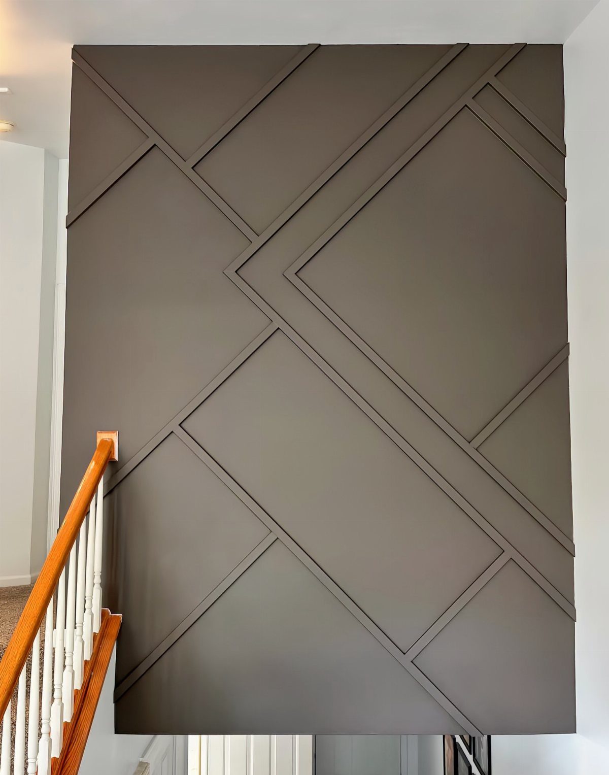 Dark grey accent wall with geometric wood molding patterns next to a stair railing