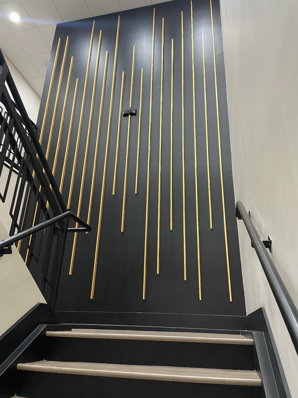 Black stairwell wall decorated with vertical gold metallic strips of different lengths.