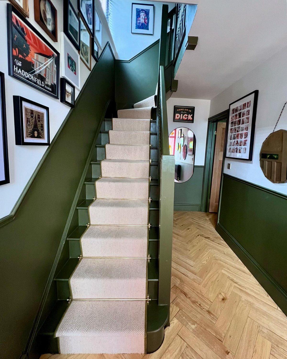Olive green paneled walls in a stairwell with beige carpet and herringbone wood floors.