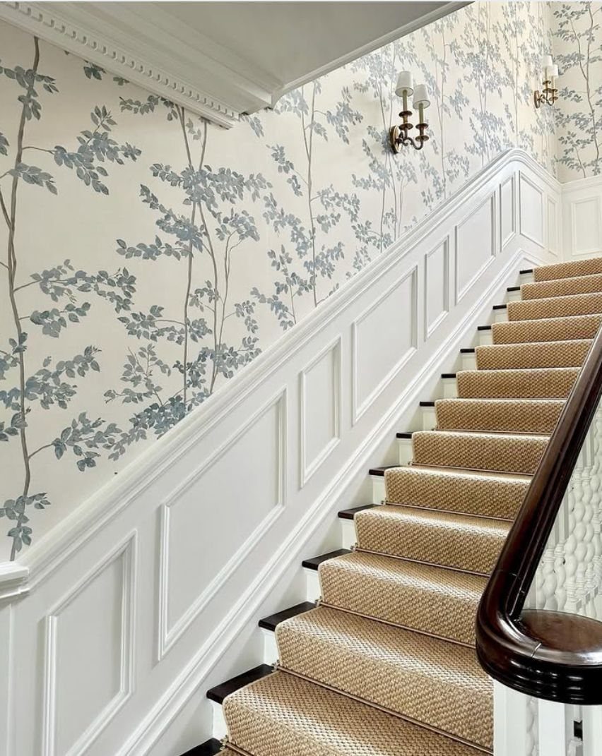 Stairwell with white wainscoting and blue floral patterned wallpaper on the accent wall.
