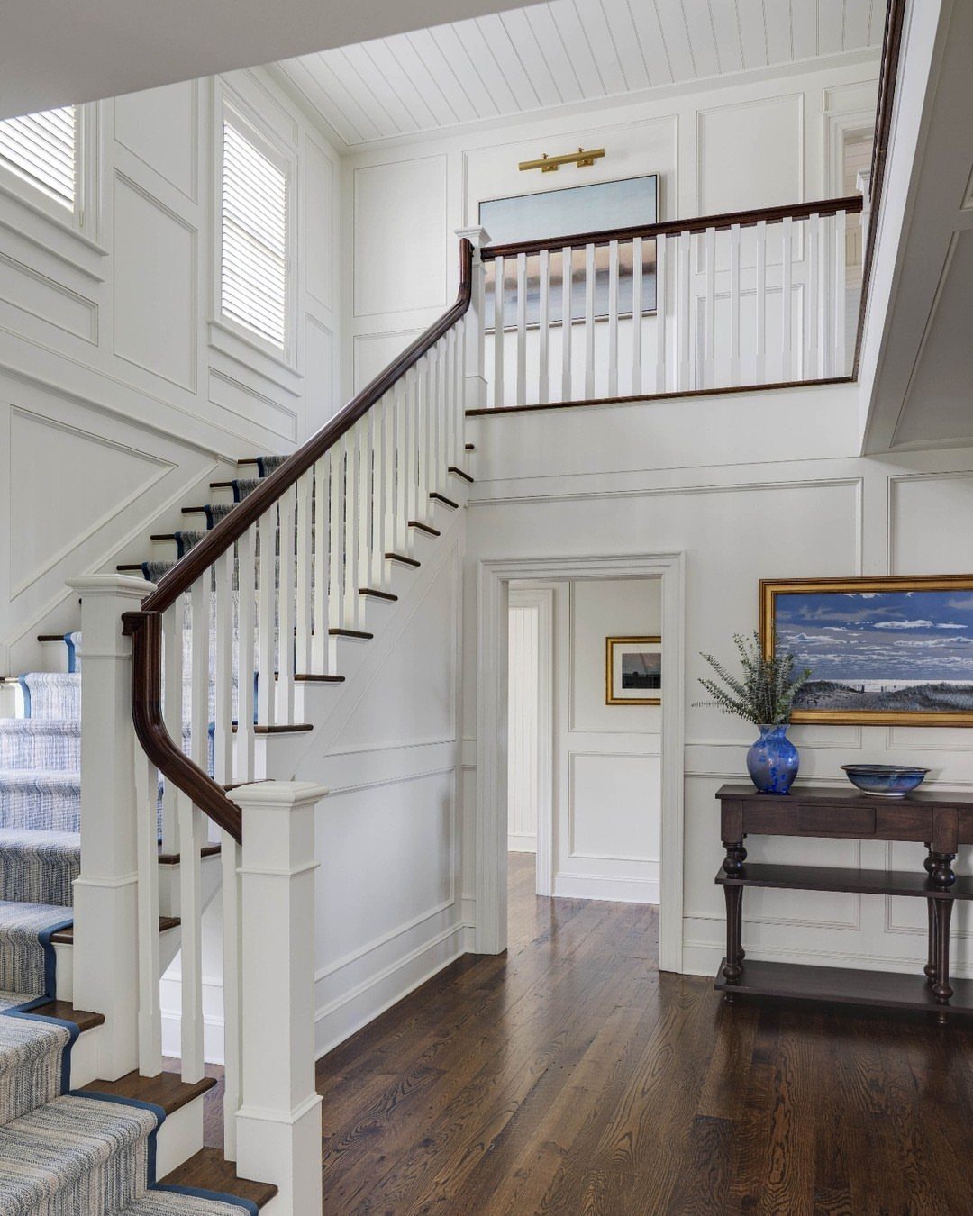 White grid paneling on the walls of a bright, traditional home stairwell.