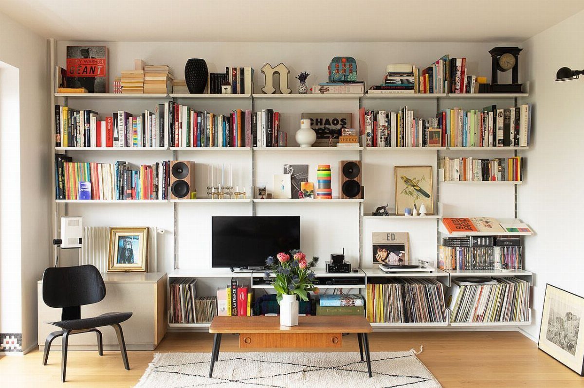39 TV Design Ideas, from Built-In Shelving to Fireplace Walls 19 Black television integrated into a large white wall-mounted bookshelf filled with colorful books.