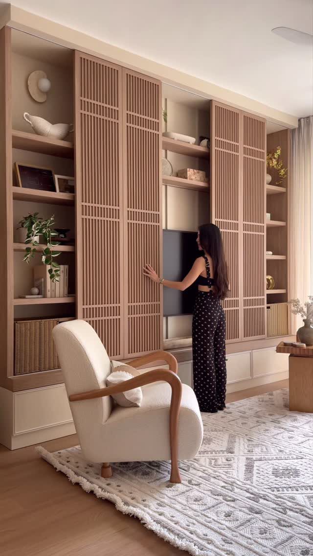 39 TV Design Ideas, from Built-In Shelving to Fireplace Walls 29 Woman standing by a light-wood built-in wall unit with slatted sliding doors hiding a TV.