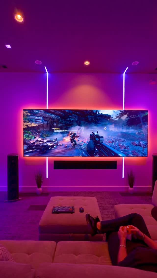 39 TV Design Ideas, from Built-In Shelving to Fireplace Walls 39 Wide television screen with purple neon accent lighting in a modern living room setup.