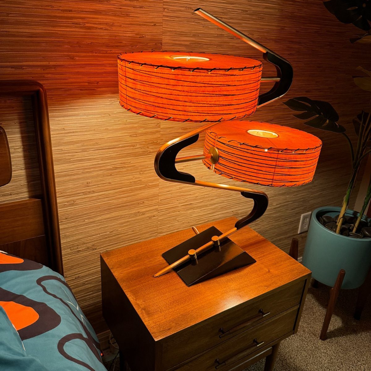 Mid-century modern lamp with orange cylindrical shades on a wooden bedside table.