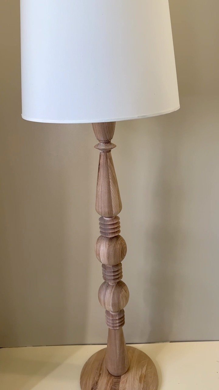 Turned natural wood lamp base with a white fabric cylindrical lampshade.