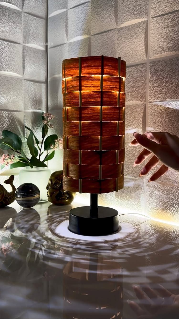 Cylindrical wooden table lamp with slatted grid design and warm glowing light.