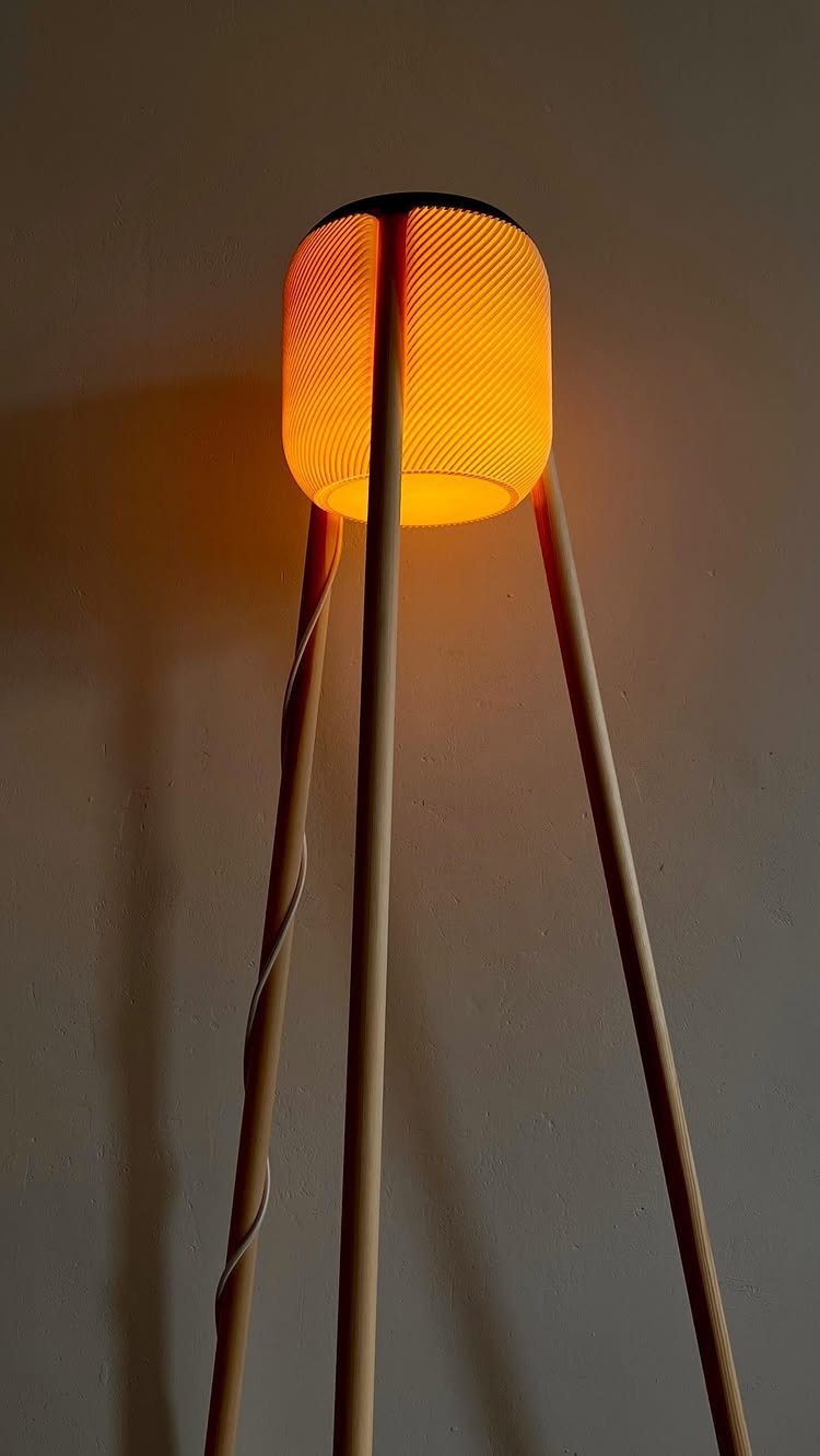 Tripod floor lamp with three wooden legs and a glowing orange cylindrical shade.