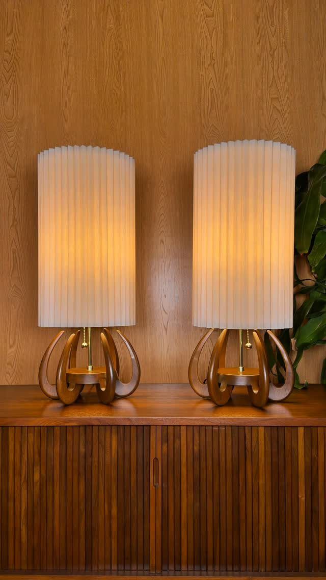 Two table lamps with white pleated shades and curved wooden bases with brass accents.