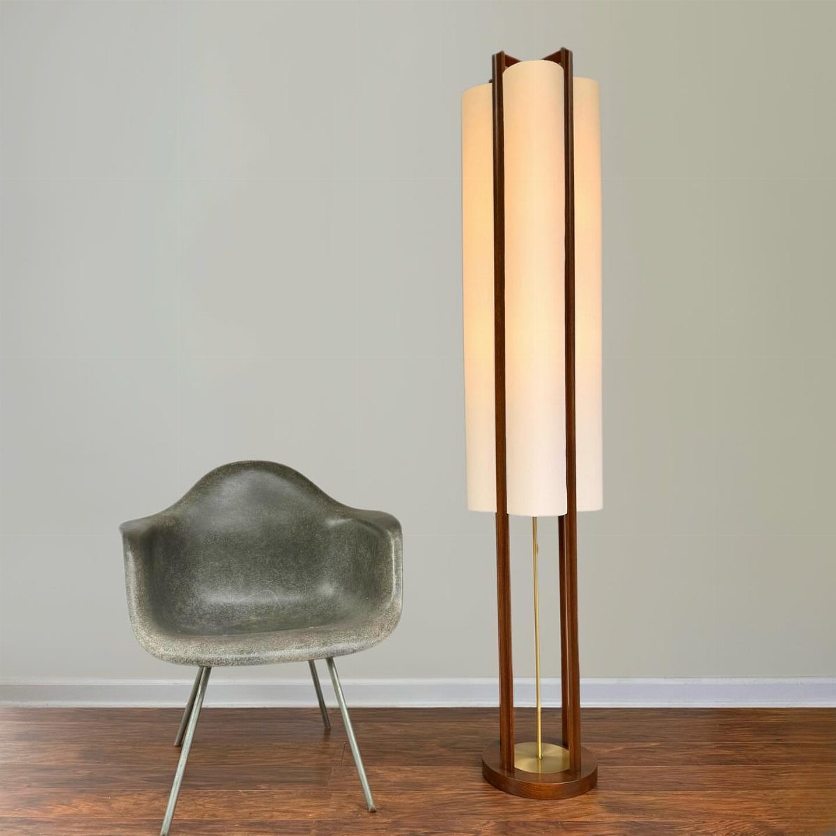 Cylindrical wooden floor lamp with white shade next to a grey modern chair.