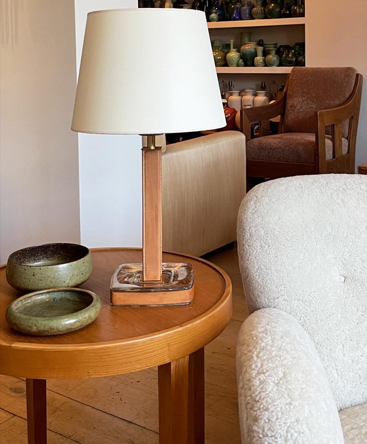 Wooden table lamp with a cream fabric shade on a round wooden side table.