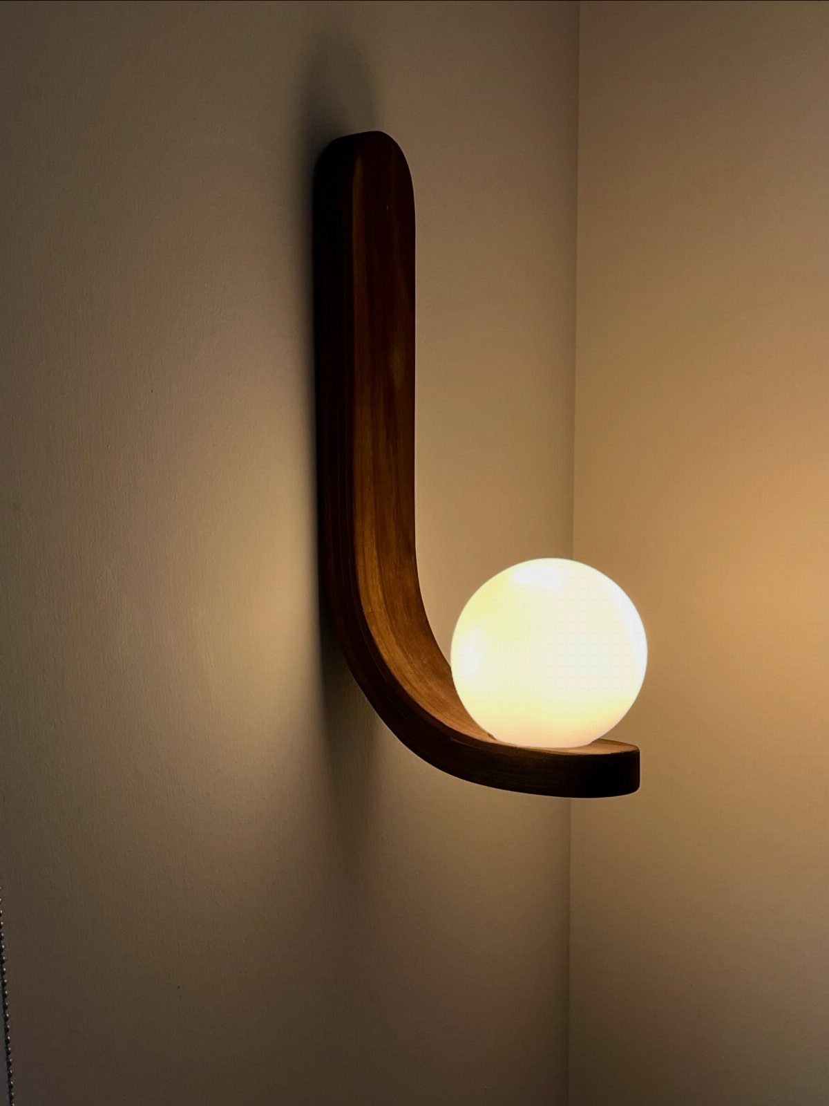 Wall-mounted wooden lamp with a curved dark brown base and glowing spherical bulb.