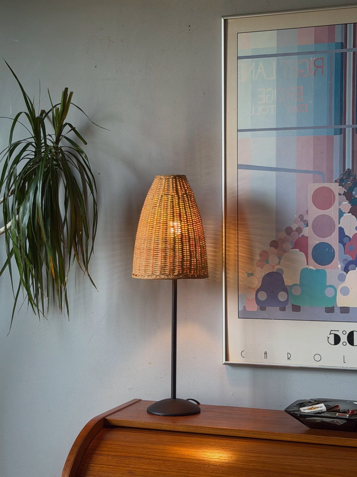 Woven wicker table lamp with a black stand on a wooden dresser.