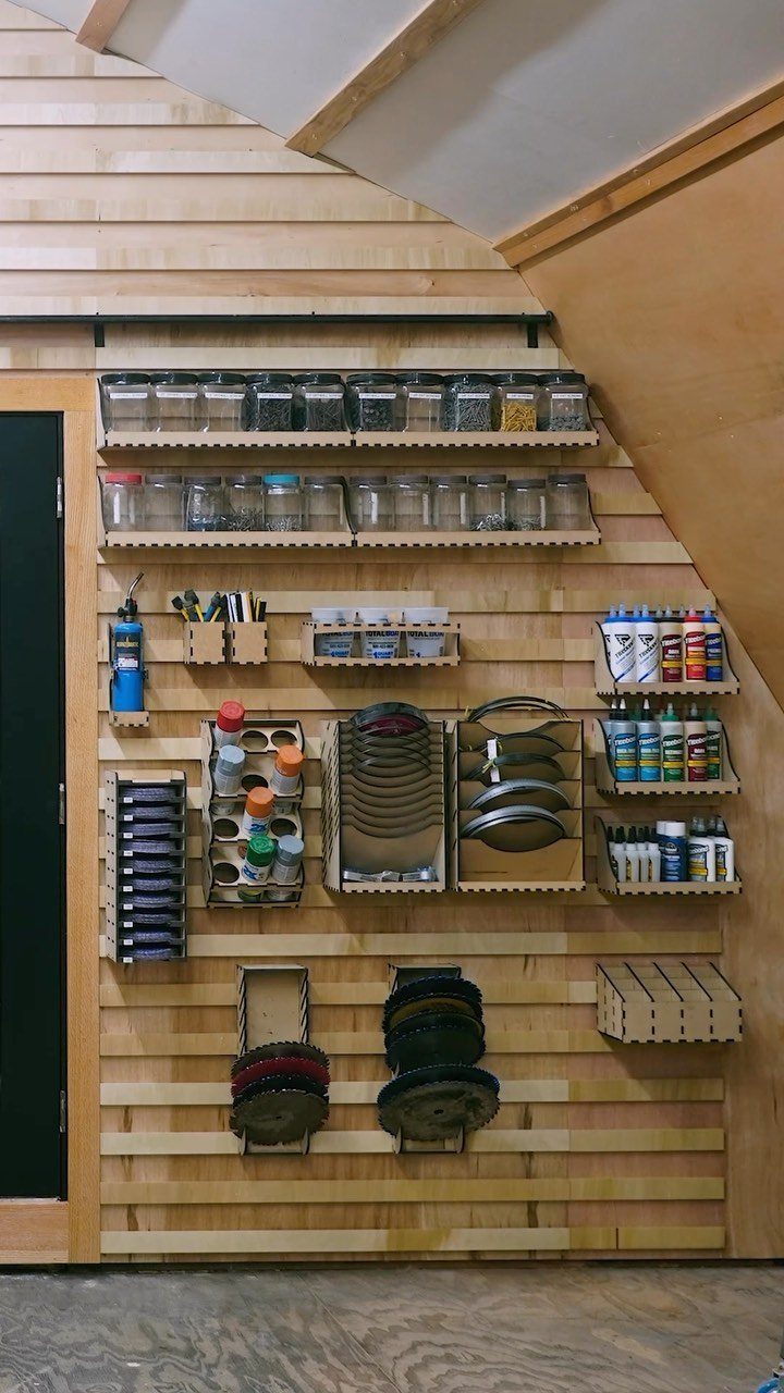 Wood Slat Wall with Shelves: 10 Ideas for Plants, TVs, Desks 1 Natural wood slat wall with adjustable shelves holding jars and workshop supplies.